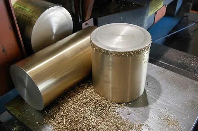 Bronze bar stock and turned part with machining swarf on a lathe bed